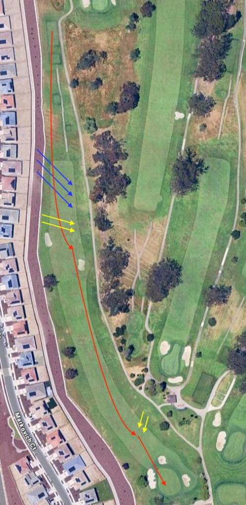 Hole 18 overhead par 5: tiered tees upper left toward green lower right along a narrow fairway, homes and cart path left and trees right, oval fairway bunkers left midway, circular green surrounded by four bunkers, red line down left side of fairway then sharp bend right into the green center, blue and yellow arrow groups from margins toward the fairway and approach suggesting wind or aim cues